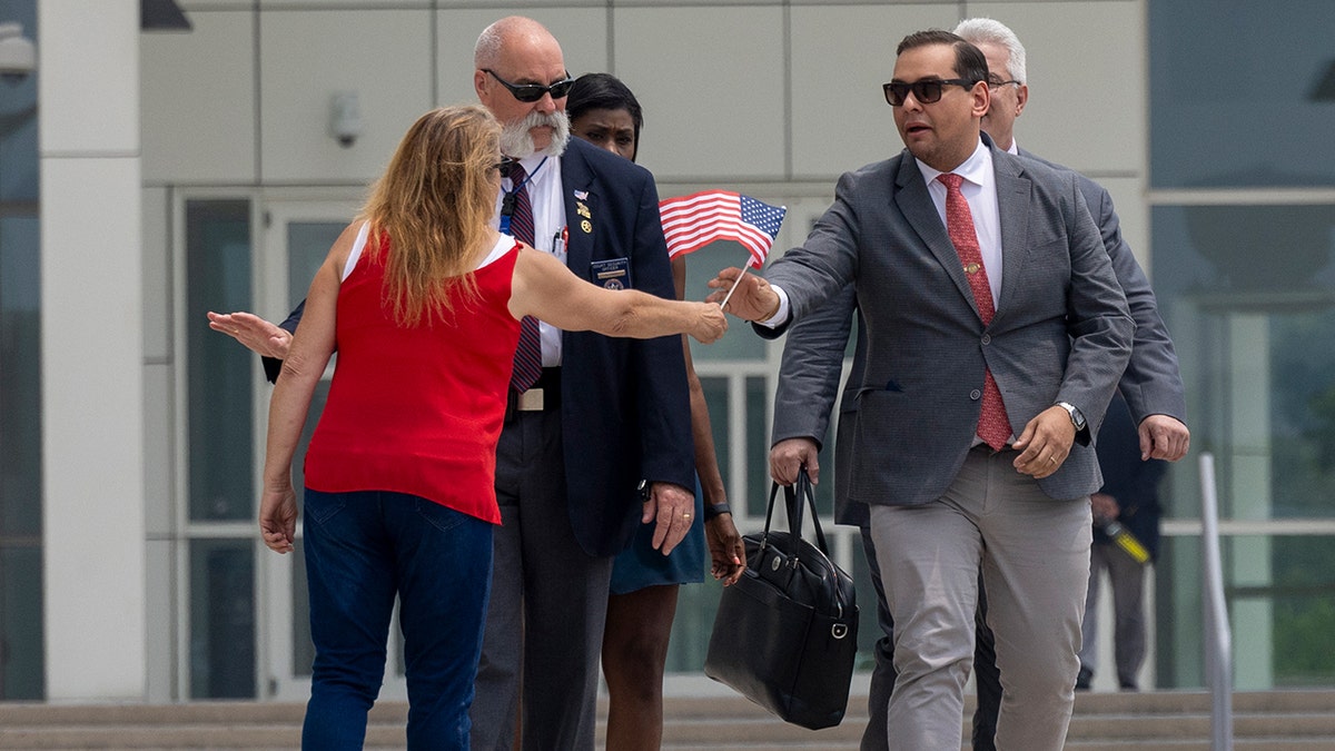 Rep. George Santos (red tie) is presented with a miniature American flag as he departs federal court