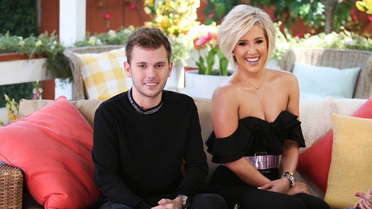 Chase and Savannah Chrisley smile and sit on the couch for a photo