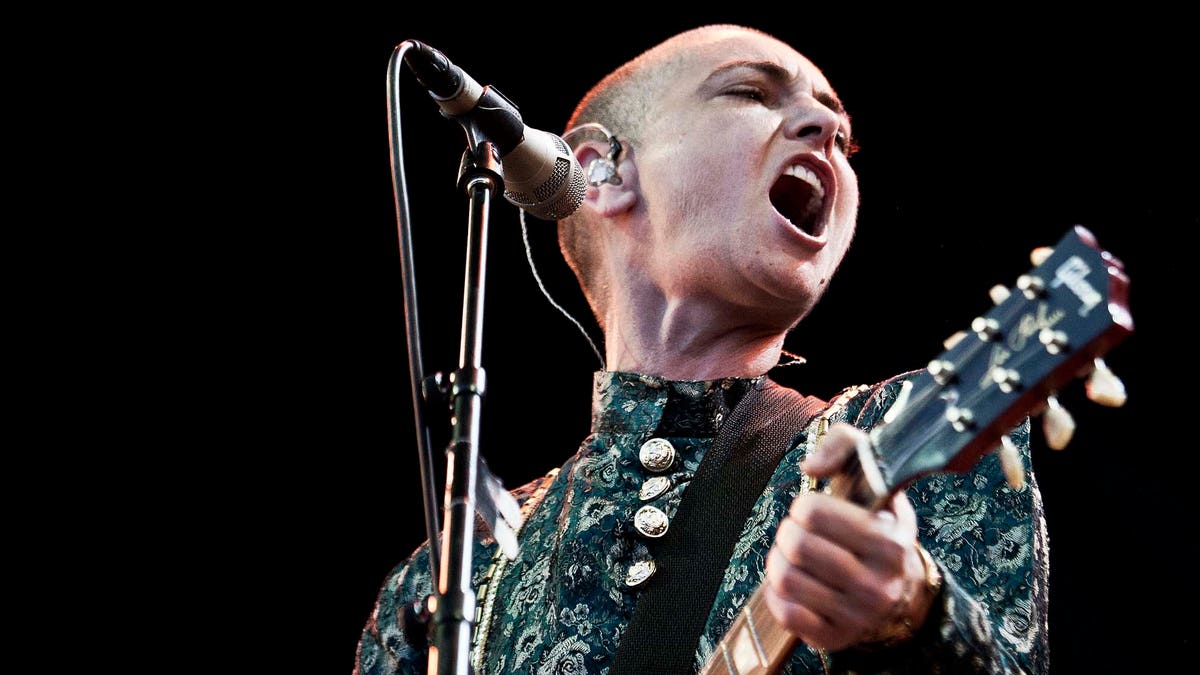 Sinéad O'Connor passionately sings on stage while holding a guitar