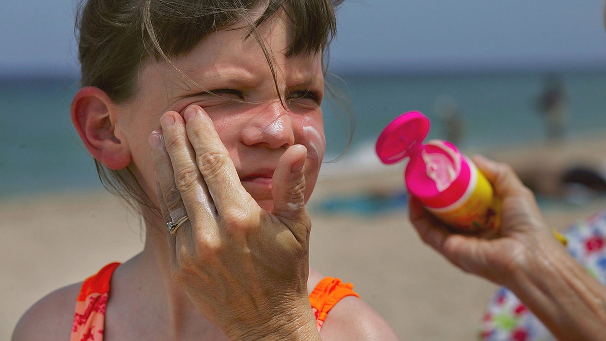 Young girl getting sunscreen applied to her face