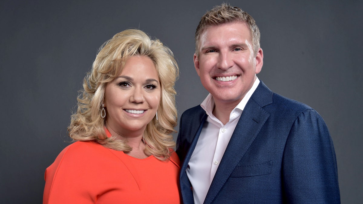 Julie Chrisley in an orangey dress smiles next to husband Todd Chrisley in a navy suit