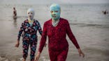 Two women in full-body swimsuits wear facekinis