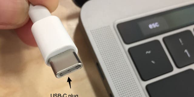 Photo of a USB-C Plug next to an Apple laptop.