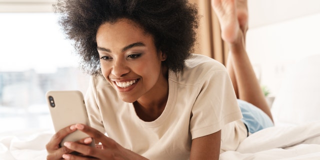 Por qué nunca debes darle a alguien tu número de teléfono en las aplicaciones de citas 4 Una mujer sonriendo y mirando su teléfono.