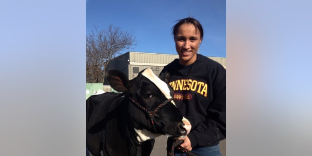 Danicka Bergeson poses next to a cow, wearing a University of Minnesota sweatshirt