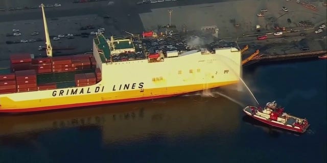 firefighter boat spraying deck of cargo ship with water