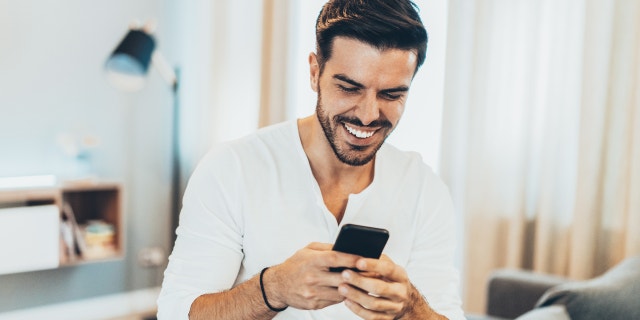 Por qué nunca debes darle a alguien tu número de teléfono en las aplicaciones de citas 5 Un hombre sonriendo y sosteniendo su teléfono.