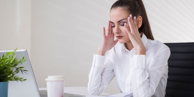 امرأة مرهقة تمسك برأسها وهي تعمل على الكمبيوتر