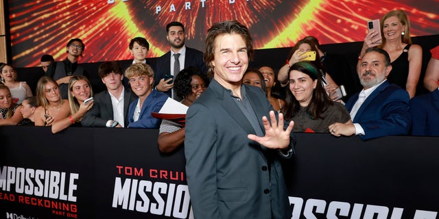 Tom Cruise stands in front of fans and waves