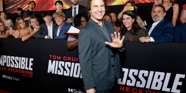 Tom Cruise stands in front of fans and waves