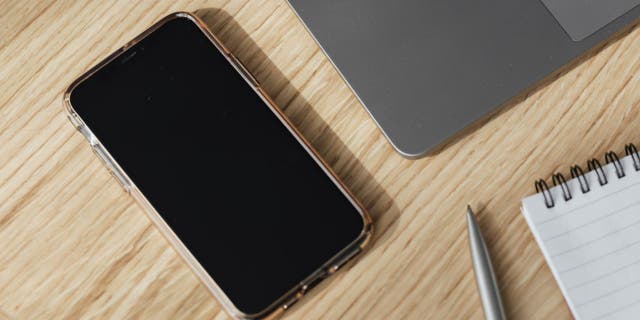 Masada koyu ekranlı iPhone, dizüstü bilgisayar ve not defteri ile