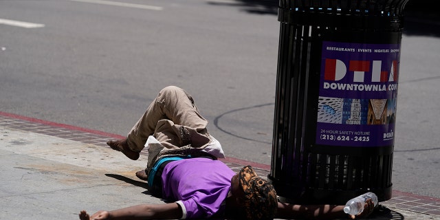 A homeless person lies on the sidewalk