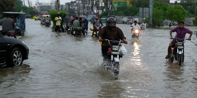 Motorcyclists drive through a flooded road