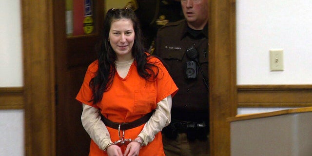 Taylor Schabusiness smiles in handcuffs and an orange jumpsuit while entering the courtroom