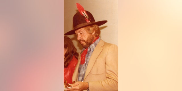 A candid photo of Buck Owens looking away while wearing a tanned suit and a hat with a feather