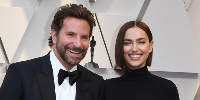 Bradley Cooper in a traditional tux and Irina Shayk in a black turtleneck dress smiles at the Oscars