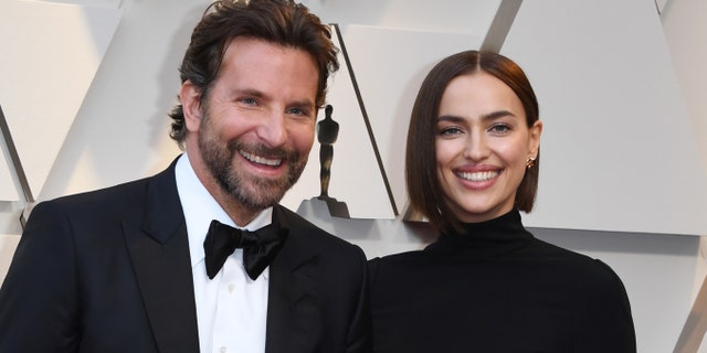 Bradley Cooper in a traditional tux and Irina Shayk in a black turtleneck dress smiles at the Oscars