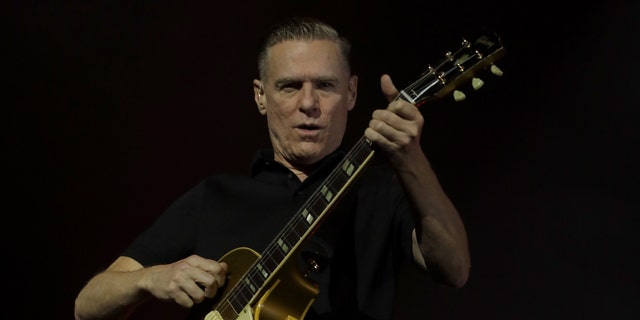 Bryan Adams strums the guitar and holds it up while performing in Auckland, New Zealand