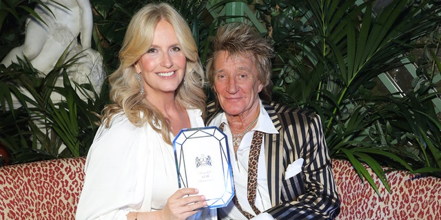 Rod Stewart in a pinstriped satin jacket with wife Penny in white