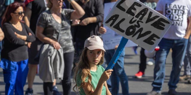 A girl holds a sign reading "Leave Us Alone"