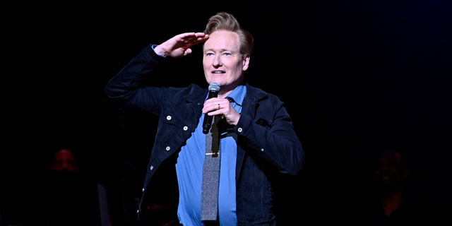 Conan O'Brien salutes the crowd on stage while holding a microphone
