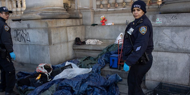 NYPD officer removes debris from homeless camp