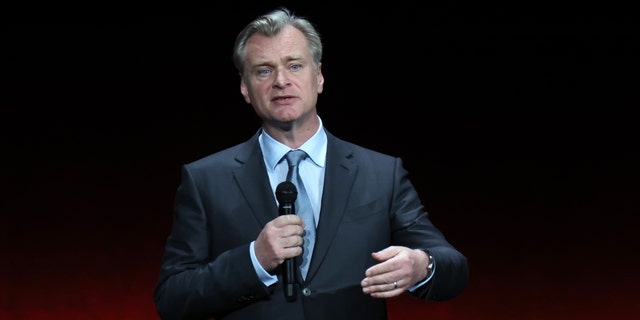 Christopher Nolan speaks on stage and holds a microphone while promoting his film "Oppenheimer" at CinemaCon in Las Vegas