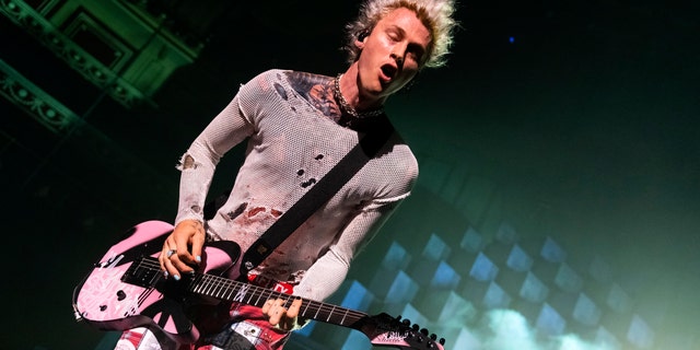 Machine Gun Kelly looks down and plays his guitar in London