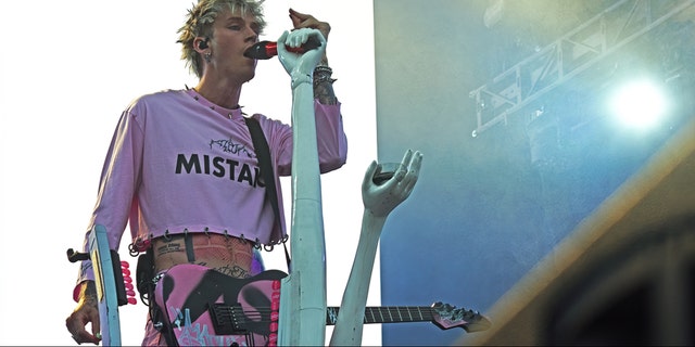 Machine Gun Kelly wearing a pink shirt sings into the microphone in the Netherlands