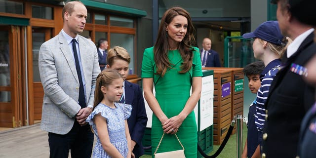 Prince William, Princess Charlotte, Prince George, and Kate Middleton talking with tennis officials