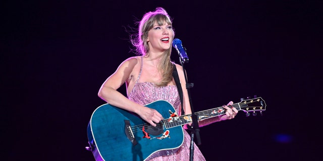 Taylor Swift in her purple dress and blue guitar playing in Denver on the Eras Tour