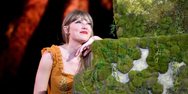 Taylor Swift looks up leaning against her moss covered piano playing in Denver