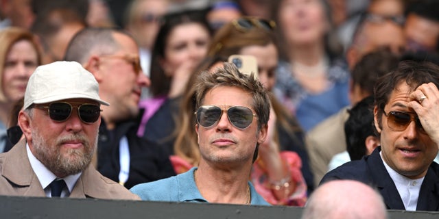 Brad Pitt wearing sunglasses and blue shirt in the stands at Wimbledon.