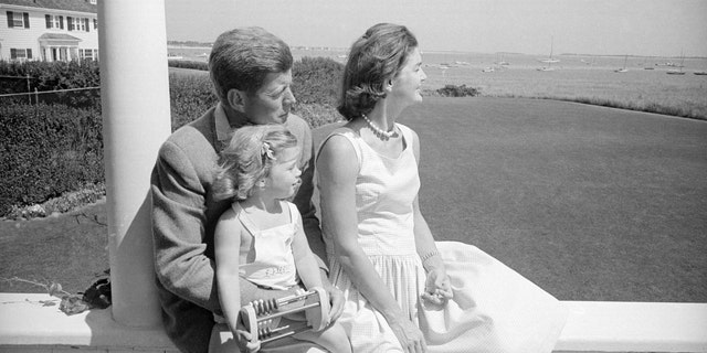 John F. Kennedy has Caroline on his lap sitting and looking out on the Cape with Jackie