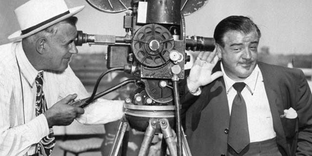Lou Costello holds ear to camera aboard the Queen Elizabeth.