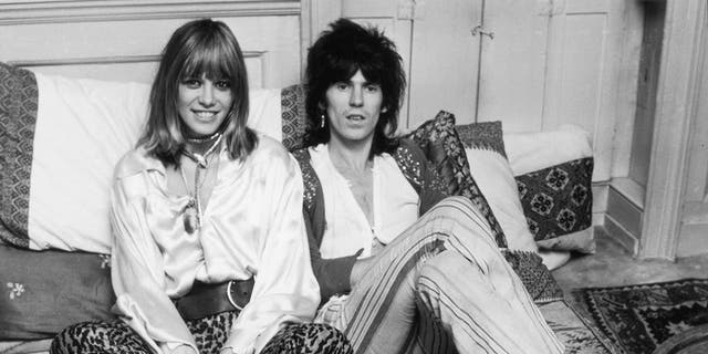 Anita Pallenberg and Keith Richards wearing white blouses and striped pants sitting in bed