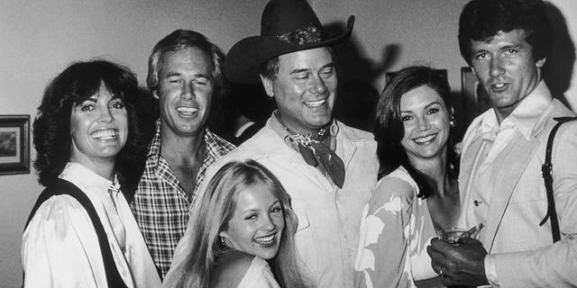 The cast members of Dallas in a black and white shot smiling with each other