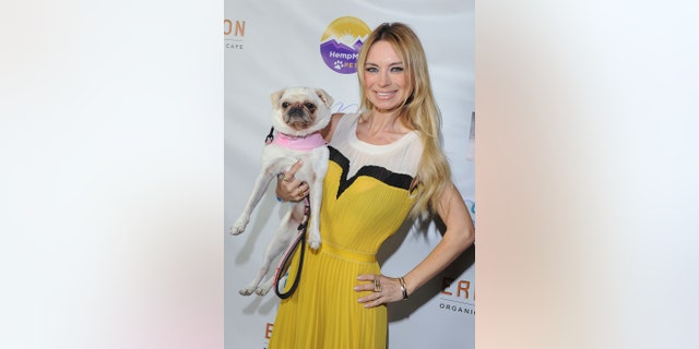 Izabella St. James wearing a yellow and white dress holding a pug