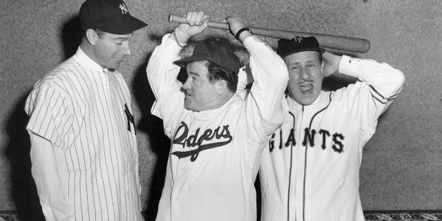 Joe DiMaggio in his baseball uniform looking at Budd Abbott and Lou Costello also in baseball uniforms and holding bats