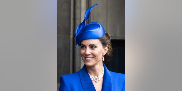 A close-up of Kate Middleton smiling wearing a blue dress and a pearl choker necklace