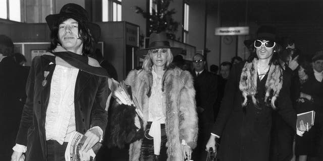 Mick Jagger, Anita Pallenberg and Keith Richards wearing coats and walking together