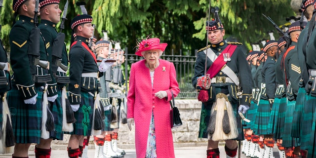 Queen Elizabeth wearing a hot pink coat with Scottish guards surrounding her