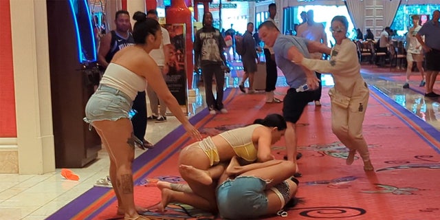 A woman in a thong is shown tussling with a woman in cut off shorts on the floor of a casino.