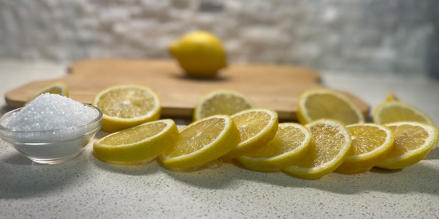 Sliced lemons and sea salt arranged in front of a wood cutting board.