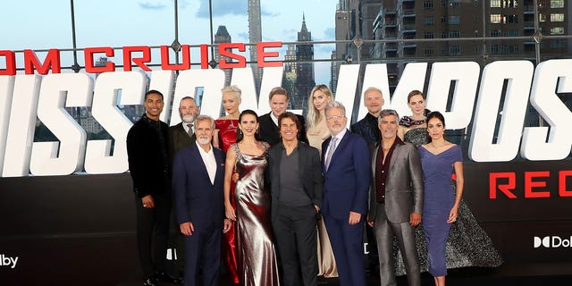 The cast of Mission: Impossible Dead Reckoning Part 1 stand together in a group, including Tom Cruise, Hayley Atwell, Simon Pegg, Rebecca Ferguson, Vanessa Kirby, and director Chris McQuarrie