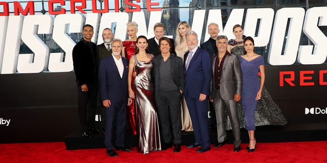 The cast of Mission: Impossible Dead Reckoning Part 1 stand together in a group, including Tom Cruise, Hayley Atwell, Simon Pegg, Rebecca Ferguson, Vanessa Kirby, and director Chris McQuarrie