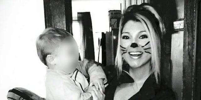 A woman with painted on whiskers holds a baby in a black-and-white photo.