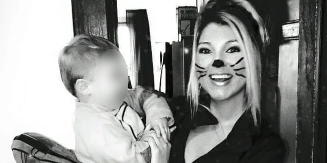 A woman with painted on whiskers holds a baby in a black-and-white photo.