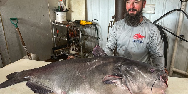 Micka Burkhart stands next to his 122-pound record catfish.