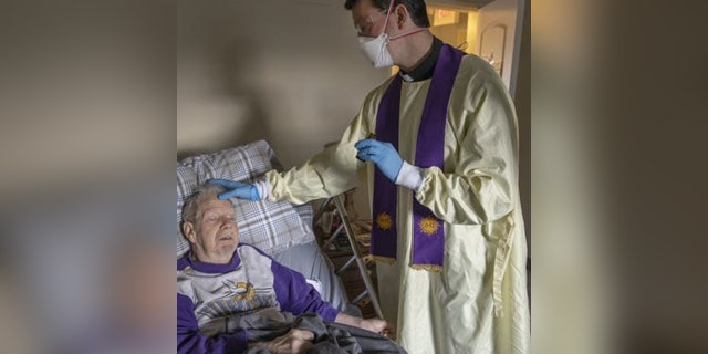 priest gives anointing of the sick to an elderly man